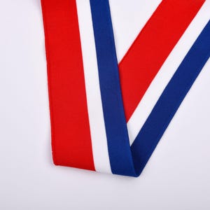 May include: A close-up shot of a ribbon with a red, white, and blue color scheme. The ribbon is folded over itself, creating a V-shape. The background is plain white.