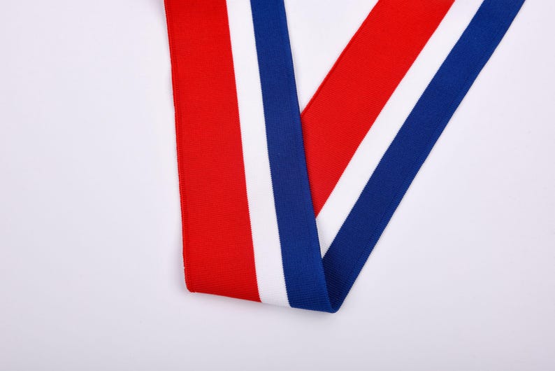 May include: A close-up shot of a ribbon with a red, white, and blue color scheme. The ribbon is folded over itself, creating a V-shape. The background is plain white.