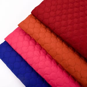Puede incluir: Cuatro piezas de tela acolchada en diferentes colores: azul, rosa, naranja y rojo. La tela tiene un patr&oacute;n acolchado de peque&ntilde;os c&iacute;rculos.