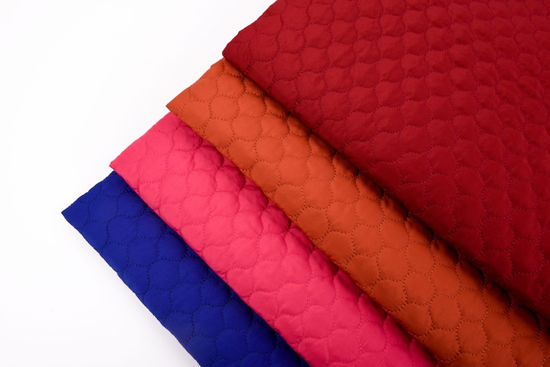 Puede incluir: Cuatro piezas de tela acolchada en diferentes colores: azul, rosa, naranja y rojo. La tela tiene un patr&oacute;n acolchado de peque&ntilde;os c&iacute;rculos.