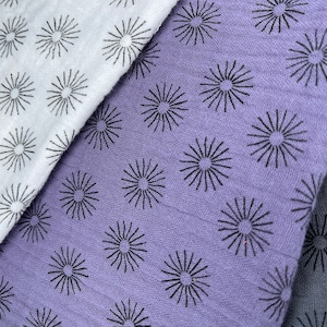 May include: Three fabric swatches with a repeating pattern of black sunburst designs. The swatches are white, light purple, and dark gray.