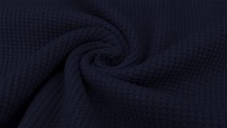 May include: Close-up of navy blue waffle knit fabric, showing a textured pattern. The fabric is swirled, creating a spiral effect. The material appears soft and pliable, with a subtle sheen.