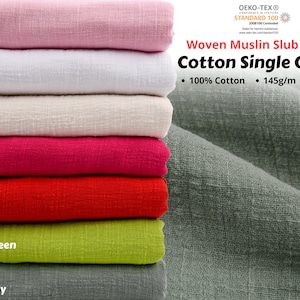 May include: A stack of woven muslin slub fabric in various colours, including pink, white, butter, fuchsia, red, apple green, and green bay. The fabric is 100% cotton, 145 grams per metre, and 132 centimetres wide. The fabric is certified by OEKO-TEX Standard 100.