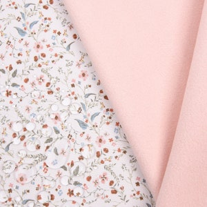 May include: A close-up of a soft shell fabric with a floral print. The fabric is water repellent, breathable, and has a TPU layer bonded to it. The fabric is pink and white.