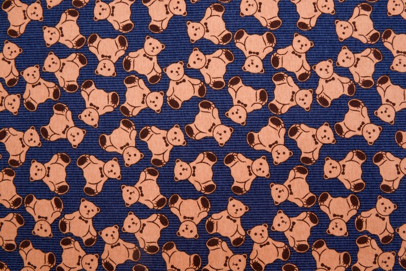 May include: A blue fabric with a repeating pattern of brown teddy bears wearing bow ties. The bears are facing different directions and are arranged in a staggered pattern.