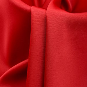 Puede incluir: Primer plano de tela roja vibrante con superficie texturizada. La tela est&aacute; drapeada y doblada, creando sombras y reflejos que enfatizan su textura suave. El efecto general es rico y lujoso.