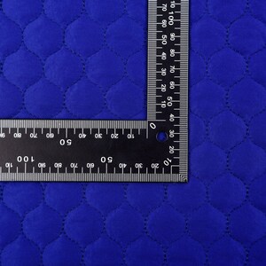 Puede incluir: Primer plano de una tela acolchada azul real con una regla que mide 100 cent&iacute;metros. La tela tiene un patr&oacute;n de diamante con un borde cosido.