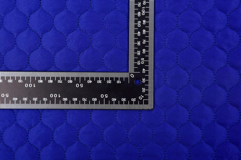 Puede incluir: Primer plano de una tela acolchada azul real con una regla que mide 100 cent&iacute;metros. La tela tiene un patr&oacute;n de diamante con un borde cosido.