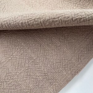 May include: Close-up of a beige fabric with a textured woven pattern. The fabric is folded over, showing the underside.