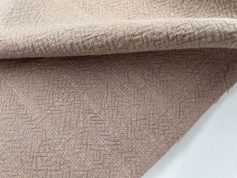May include: Close-up of a beige fabric with a textured woven pattern. The fabric is folded over, showing the underside.
