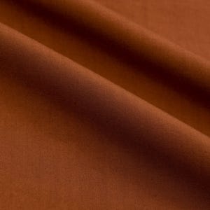 May include: Close-up of a smooth, brown fabric with a subtle sheen. The fabric is folded in a way that creates soft, flowing lines.