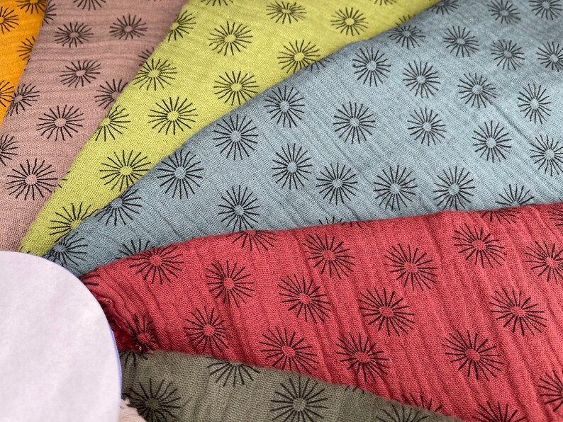 May include: A collection of fabric swatches with a repeating pattern of black starbursts on different colored backgrounds. The colors include brown, green, blue, red, and a light brown.