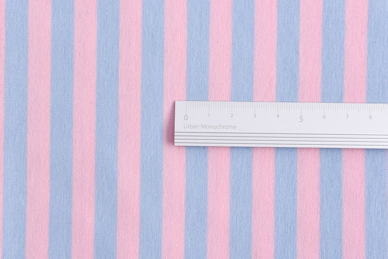 May include: A close-up of a pink and light blue striped fabric with a ruler measuring 8 inches long.