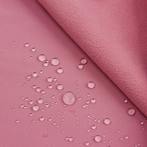 K&ouml;nnte beinhalten: Nahaufnahme eines staubrosafarbenen Stoffes mit Wassertropfen. Der Stoff hat eine glatte Seite und eine strukturierte, fleeceartige Seite. Die Wassertropfen sind unterschiedlich gro&szlig;.