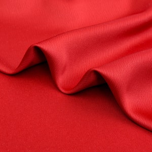 Puede incluir: Primer plano de una tela roja vibrante con pliegues suaves y un brillo sutil. El material parece liso y lujoso, con una ligera textura visible a la luz. La tela probablemente se utiliza para ropa o decoraci&oacute;n del hogar.