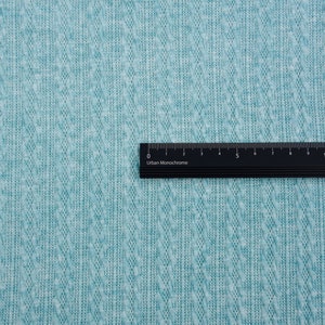 May include: A close-up of a teal textured fabric with a black ruler labeled "Urban Monochrome" placed on top. The ruler is marked in centimeters from 0 to 14.