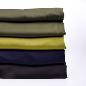 Puede incluir: Una pila de tela doblada en tonos de verde, oliva, chartreuse, azul marino y gris oscuro. La tela parece ser de un material liso y de color s&oacute;lido, posiblemente para proyectos de costura o manualidades. Los colores est&aacute;n dispuestos en gradiente de arriba a abajo.