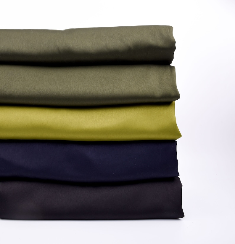 Puede incluir: Una pila de tela doblada en tonos de verde, oliva, chartreuse, azul marino y gris oscuro. La tela parece ser de un material liso y de color s&oacute;lido, posiblemente para proyectos de costura o manualidades. Los colores est&aacute;n dispuestos en gradiente de arriba a abajo.