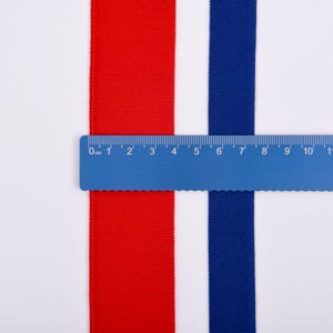 May include: A blue ruler measures red and blue fabric strips against a white background. The red strip is on the left, the blue strip is on the right, and the ruler spans 14 inches. The fabric appears to be a woven material.