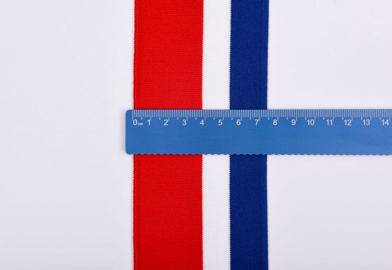 May include: A blue ruler measures red and blue fabric strips against a white background. The red strip is on the left, the blue strip is on the right, and the ruler spans 14 inches. The fabric appears to be a woven material.
