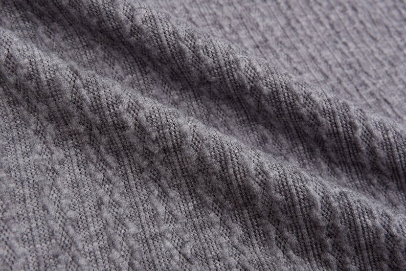 May include: Close-up of a gray knitted fabric with a textured pattern.