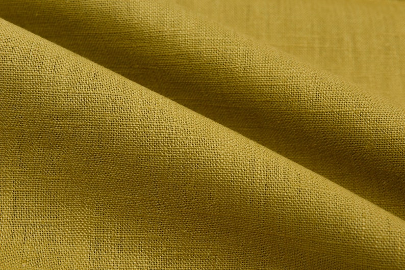 Op de afbeelding: Close-up van een textuurrijke, mosterdgele stof. De stof heeft een geweven uiterlijk en een subtiele glans.