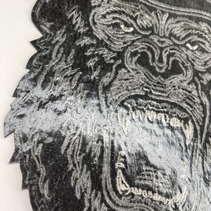 May include: Close-up of a black and white embroidered patch of a gorilla's face with a large open mouth and sharp teeth.