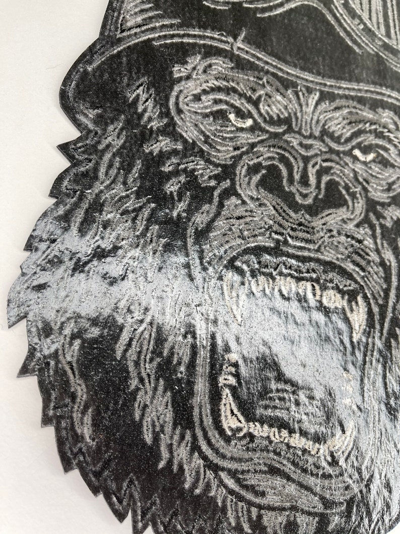 May include: Close-up of a black and white embroidered patch of a gorilla's face with a large open mouth and sharp teeth.