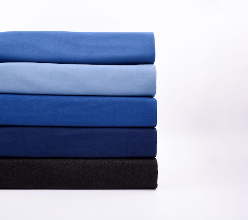 May include: A stack of folded fabric in shades of blue, ranging from light to dark. The colors include light blue, medium blue, navy, and black. The fabric appears to be a soft material, possibly cotton or linen.