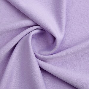 Pode incluir: Close-up de um tecido macio e liso de cor lavanda com uma textura sutil. O tecido est&aacute; dobrado e drapeado, criando uma curva suave.