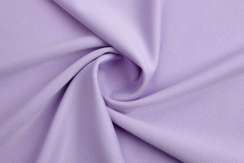 Pode incluir: Close-up de um tecido macio e liso de cor lavanda com uma textura sutil. O tecido est&aacute; dobrado e drapeado, criando uma curva suave.