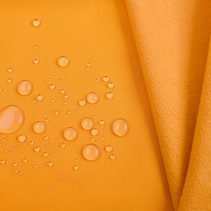 K&ouml;nnte beinhalten: Nahaufnahme eines goldgelben Stoffes mit Wassertropfen auf der Oberfl&auml;che. Ein Teil des Stoffes ist gefaltet und zeigt seine Textur. Die Tropfen sind unterschiedlich gro&szlig; und erzeugen einen dynamischen visuellen Effekt. Der Stoff wirkt weich.