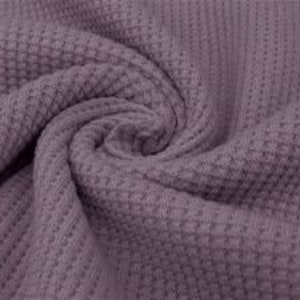 May include: Close-up of a swirl of mauve-colored waffle knit fabric. The fabric has a textured, grid-like pattern, with a soft, slightly blurred appearance. The folds and curves of the fabric create a sense of depth and movement.