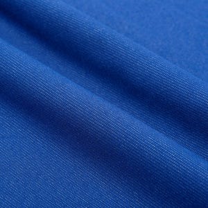 May include: Close-up of a vibrant blue fabric with a subtle textured weave. The material is folded, creating soft shadows and highlighting the detailed surface. The color is a rich, saturated blue.