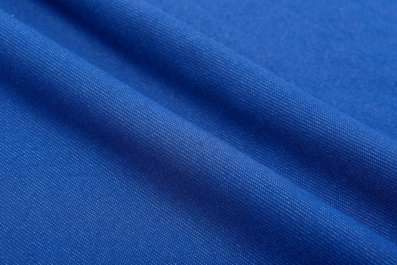 May include: Close-up of a vibrant blue fabric with a subtle textured weave. The material is folded, creating soft shadows and highlighting the detailed surface. The color is a rich, saturated blue.