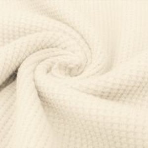May include: Close-up of a cream-colored, textured fabric with a waffle-weave pattern. The fabric is swirled, creating a spiral effect. The material appears soft and pliable, with subtle variations in tone.