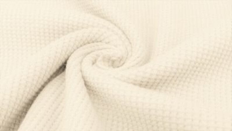 May include: Close-up of a cream-colored, textured fabric with a waffle-weave pattern. The fabric is swirled, creating a spiral effect. The material appears soft and pliable, with subtle variations in tone.