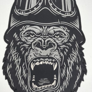 May include: A black and silver embroidered patch of a gorilla wearing a helmet and goggles. The gorilla is roaring with its mouth open, showing its teeth.