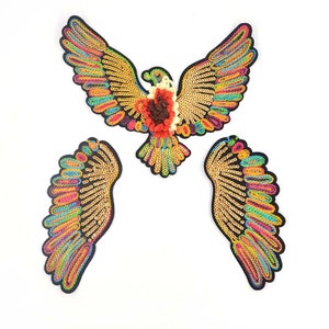 May include: Three colorful embroidered patches featuring a bird with outstretched wings. The bird is gold with rainbow colored sequins and a red and brown flower on its chest. The wings are separate and can be used individually.