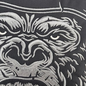 May include: Close-up of a silver embroidered gorilla face with an open mouth, showing teeth. The gorilla is on a black fabric background.