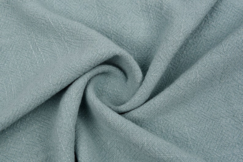 May include: A close-up of a soft, blue fabric with a textured weave. The fabric is folded and draped, showing its texture and drape.