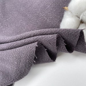 May include: Close-up of a textured, dark gray fabric with a subtle herringbone pattern. The fabric is folded and draped, showcasing its soft and drapey texture.