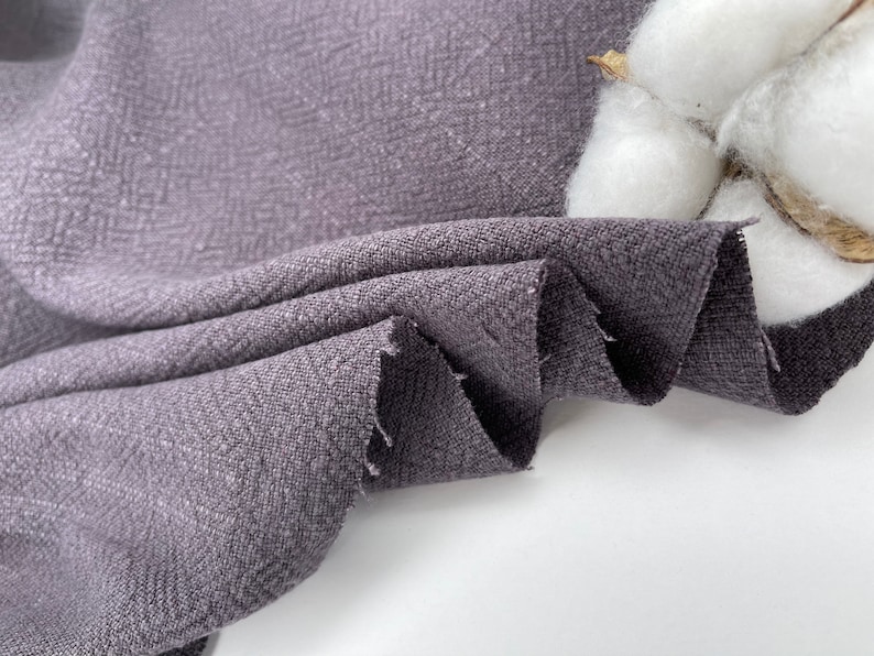 May include: Close-up of a textured, dark gray fabric with a subtle herringbone pattern. The fabric is folded and draped, showcasing its soft and drapey texture.