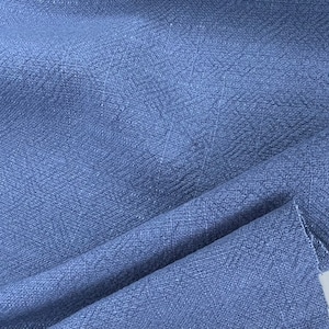 May include: Close-up of a blue textured fabric with a subtle herringbone pattern. The fabric is folded and draped, showcasing its soft and drapey texture.