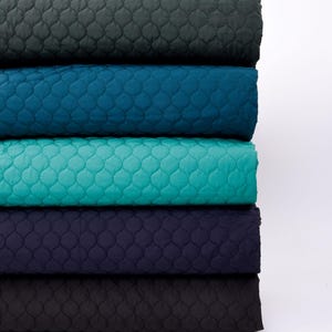 Puede incluir: Cinco rollos de tela acolchada en diferentes colores: verde oscuro, azul verdoso, turquesa, azul marino y negro. La tela tiene un patr&oacute;n de diamante.
