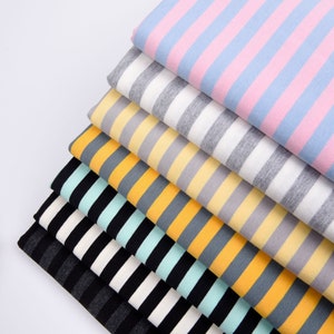 May include: A stack of striped fabric in various colors, including pink, gray, yellow, orange, and green. The fabric is folded neatly and arranged in a pyramid shape.