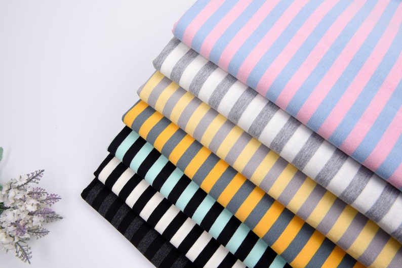May include: A stack of striped fabric in various colors, including pink, gray, yellow, orange, and green. The fabric is folded neatly and arranged in a pyramid shape.