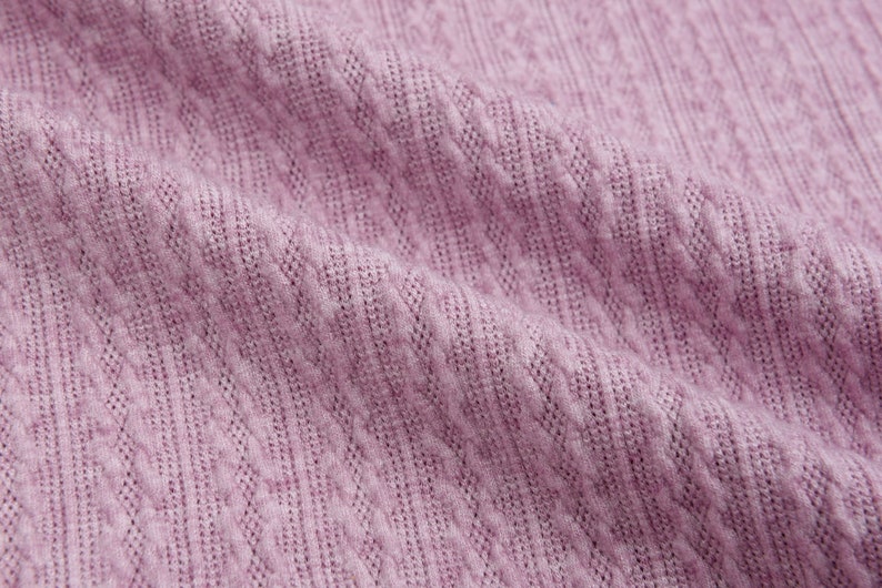 May include: Close-up of a soft, textured fabric in a light purple color. The fabric has a subtle, woven pattern.