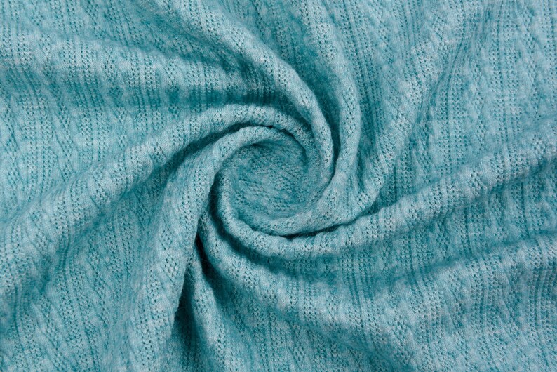 May include: A close-up of a teal blue knitted fabric with a textured pattern. The fabric is folded and twisted, creating a swirling effect.