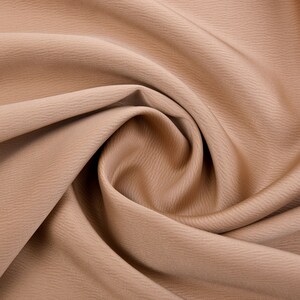 Puede incluir: Primer plano de una tela color beige con una superficie texturizada. La tela est&aacute; drapeada y arremolinada, creando pliegues y sombras suaves. El color es un tono c&aacute;lido y neutro, adecuado para diversos proyectos de costura y artesan&iacute;a.
